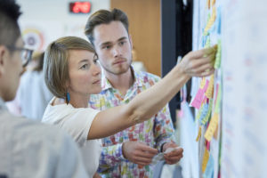 Woman posting sticky notes to idea board alongside students