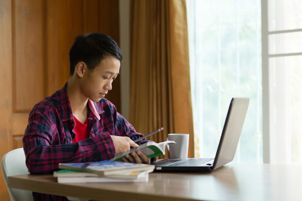 International student studying at home while using a laptop and phone
