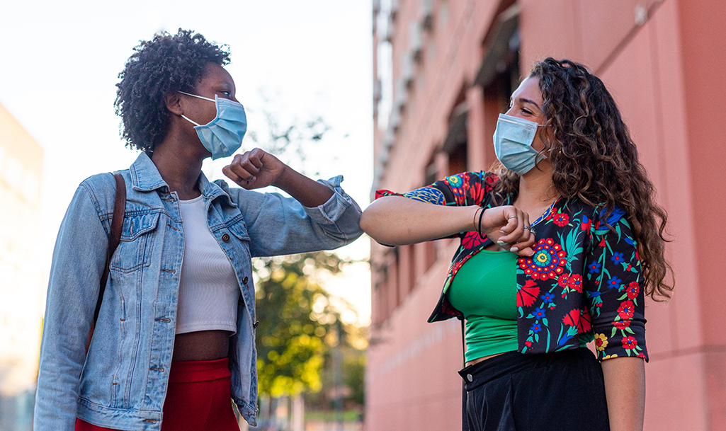 Two young women greeting each other by bumping elbows 