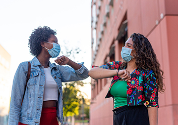 Two women doing an elbow shake with masks on