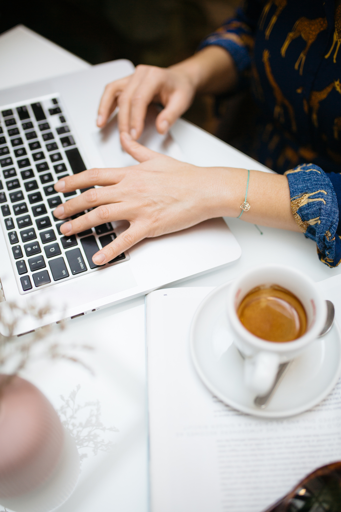 Woman working on laptop beside cup of coffee, hand on keyboard close up