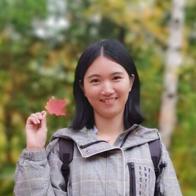 Yanling Zhuang holding a maple leaf and smiling at the camera 