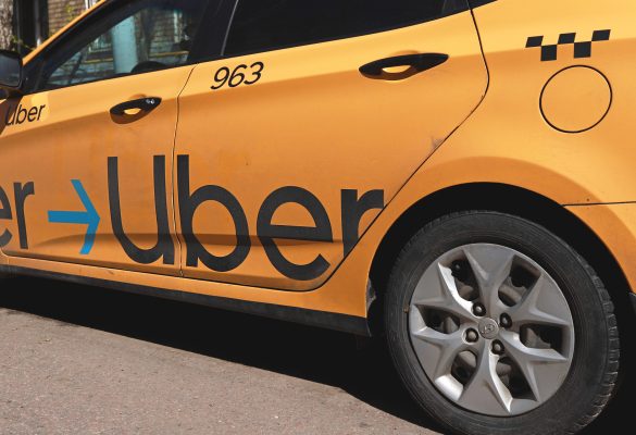 Yellow taxi with Uber logo on the street. Yellow taxi cab with checker pattern. Uber taxi cab.