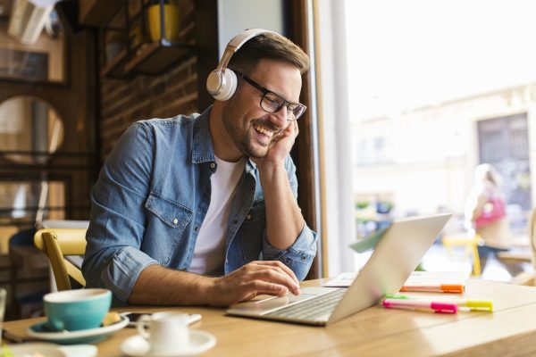 Man wearing headphones smiling at his laptop in a coffee shop