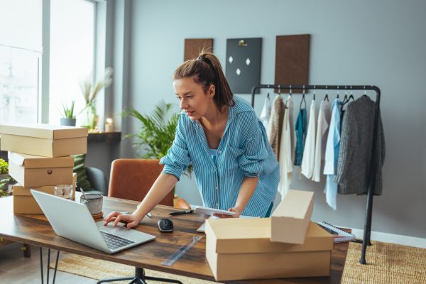 Woman checking orders on her laptop surrounded by boxes, working at her small business.