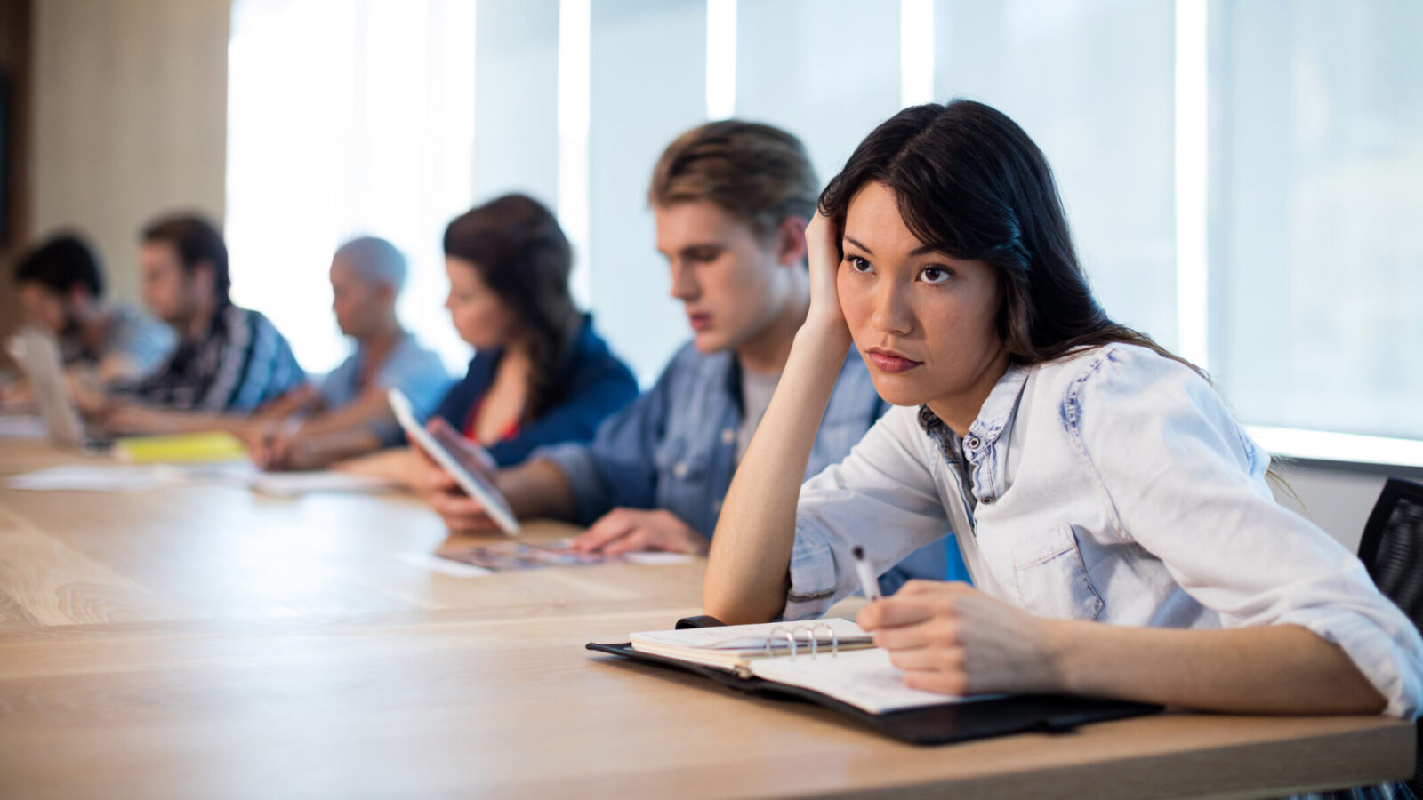 Bored woman sitting in meeting room with her colleagues