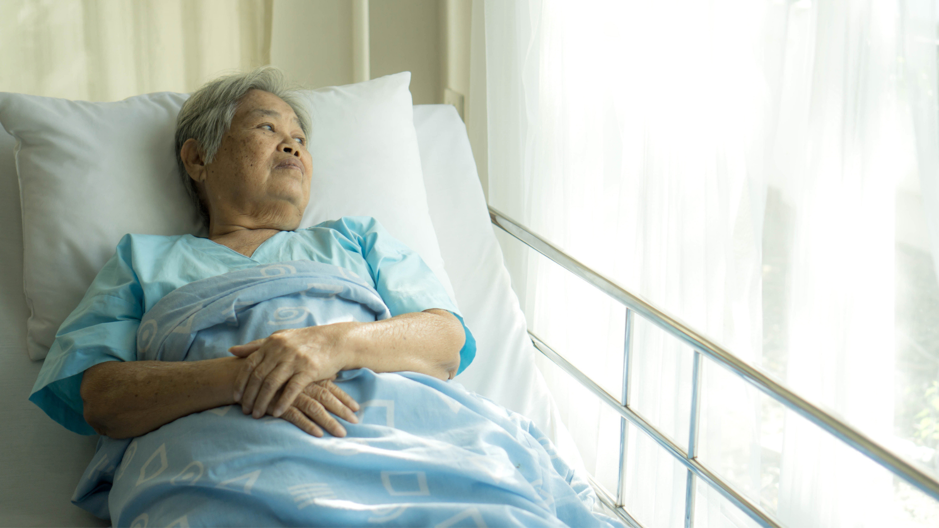 Lonely senior in a hospital bed looking out the window.