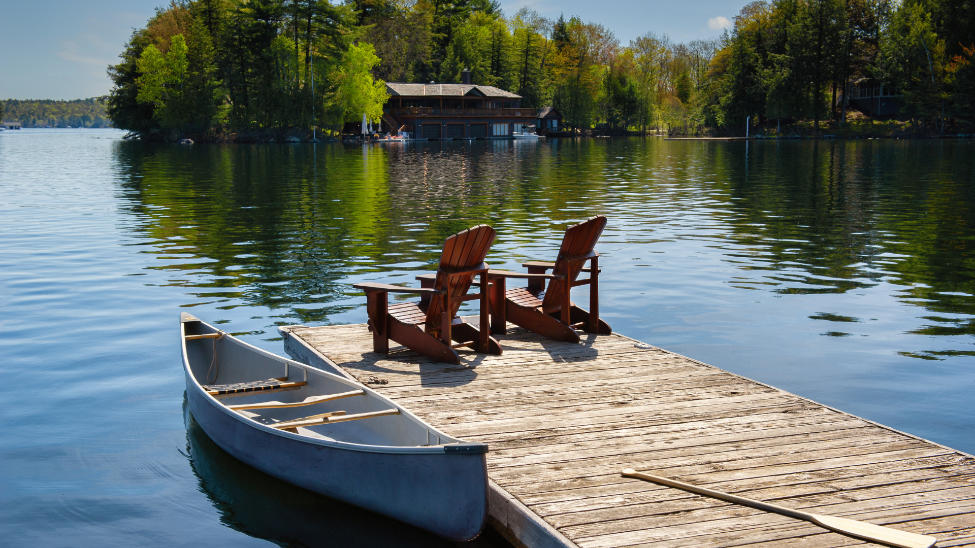 Muskoka chairs sitting on a wood dock facing a calm lake